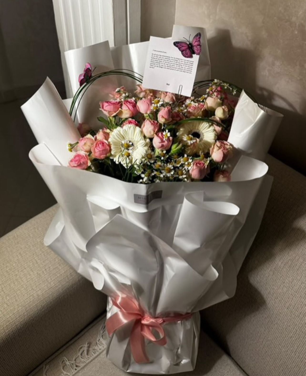 Bouquet of flowers wrapped in white paper with a pink bow on a light-colored surface.